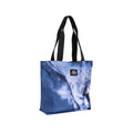 A blue tote bag featuring a printed close-up lion face design and black shoulder straps, photographed against a plain white studio background.