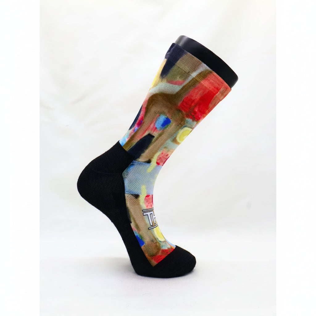 Trail socks with mohair cushioning. Single crew sock with a black toe, heel, and cuff, featuring a colorful abstract paint-splatter pattern on the leg and foot, displayed on a white background.